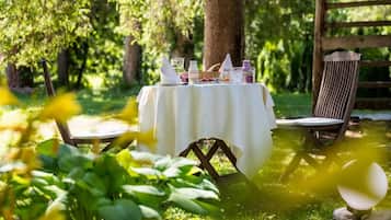 Una mesa al aire libre con mantel blanco, rodeada de follaje y una valla de madera.
