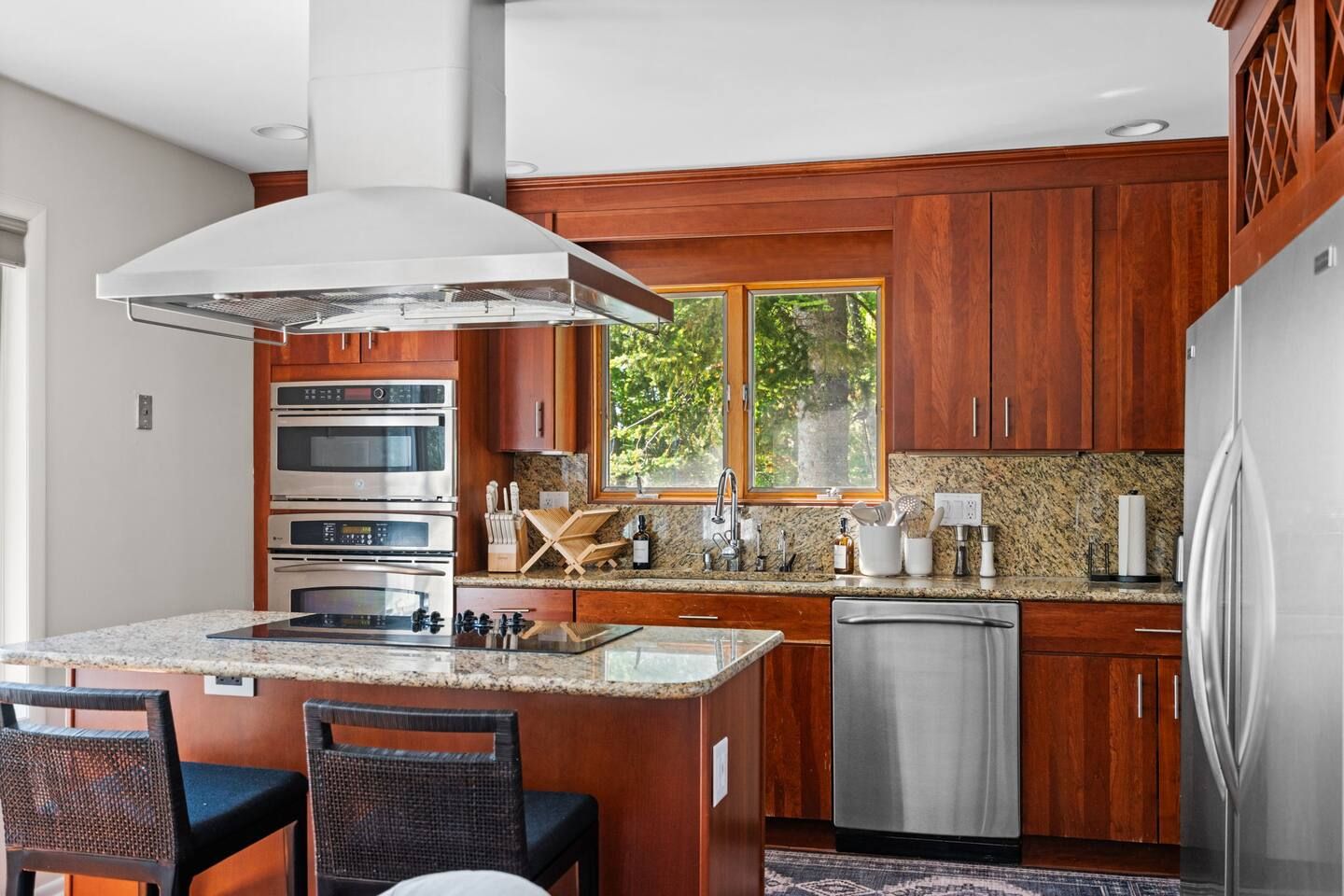 A modern kitchen with a central island, built-in ovens, a dishwasher, and wooden cabinetry.