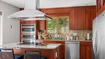 A modern kitchen with a central island, built-in ovens, a dishwasher, and wooden cabinetry.
