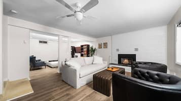 A modern living room with a white sofa, a black leather chair, a fireplace, and a ceiling fan.