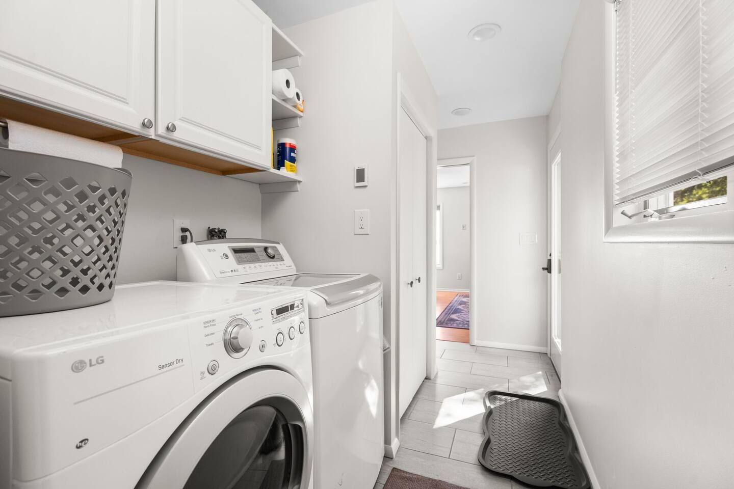 A laundry room with a front-loading washer and dryer, a basket, and a shelf with laundry supplies.
