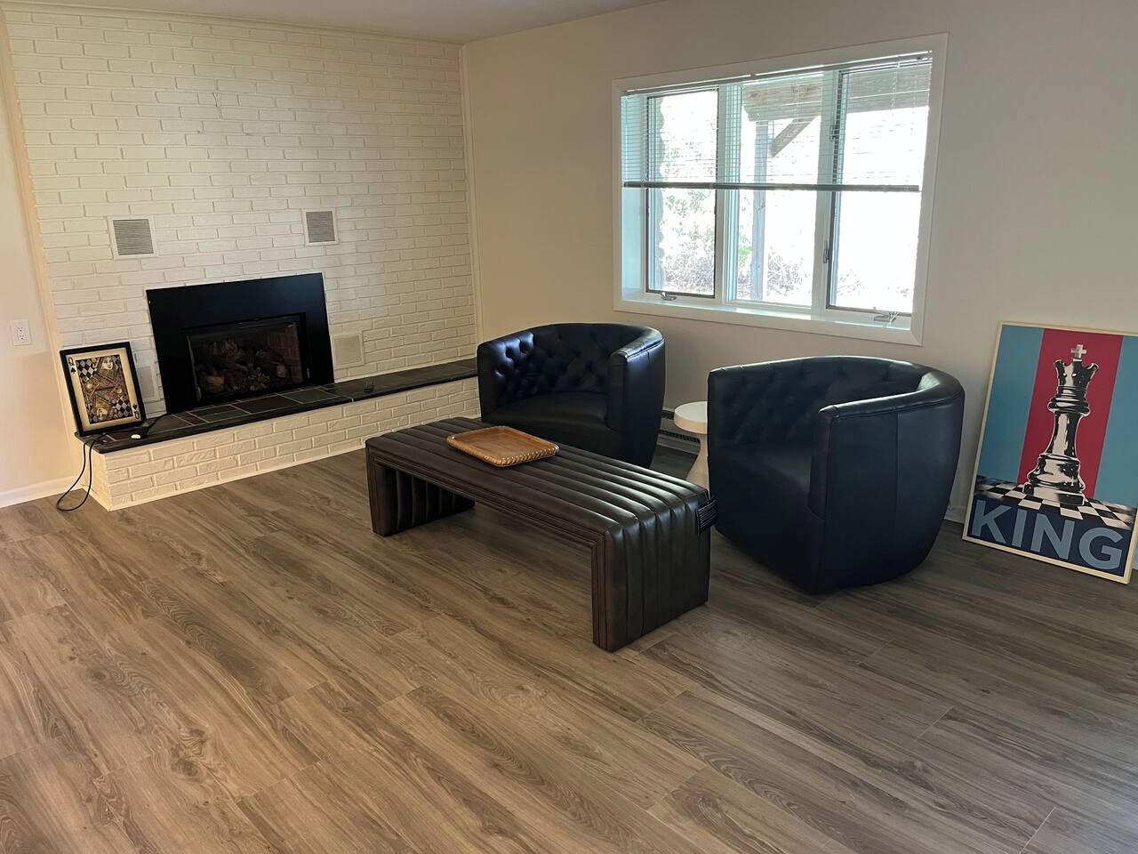 A living room with a fireplace, two black leather chairs, a wooden coffee table, and a chess-themed artwork.
