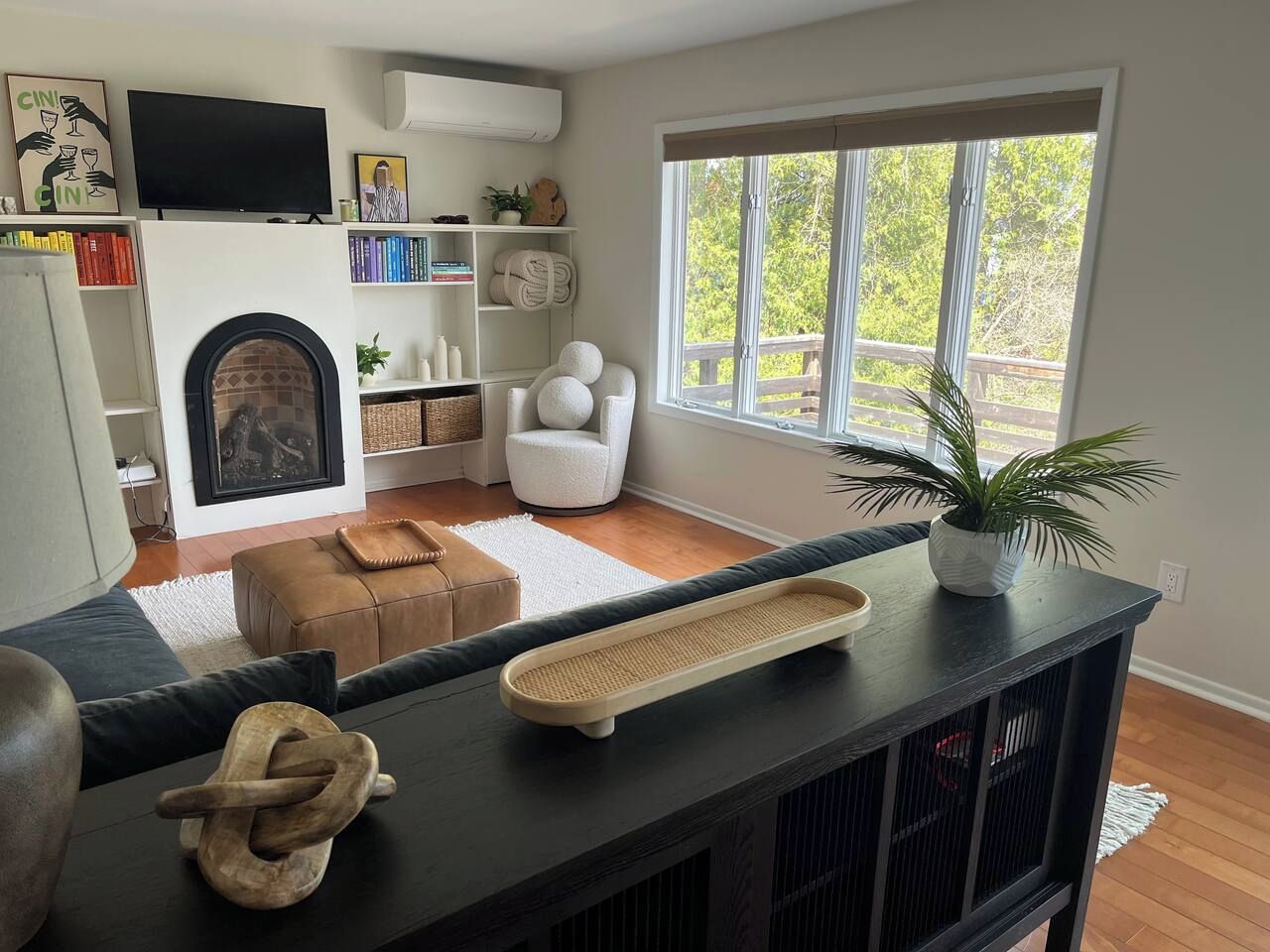 Een woonkamer met een open haard, een bank, een salontafel en een groot raam met uitzicht op bomen.