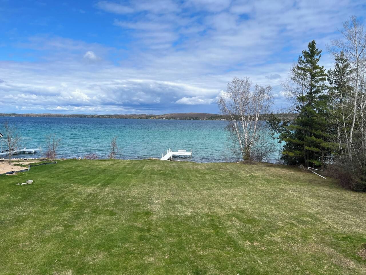 A grassy area with a dock extending into a body of water, surrounded by trees.
