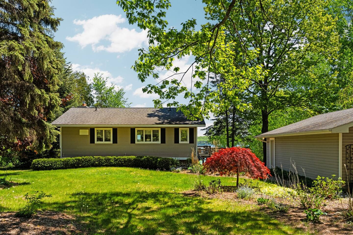 A two-story house with a well-maintained lawn and a variety of trees and shrubs.