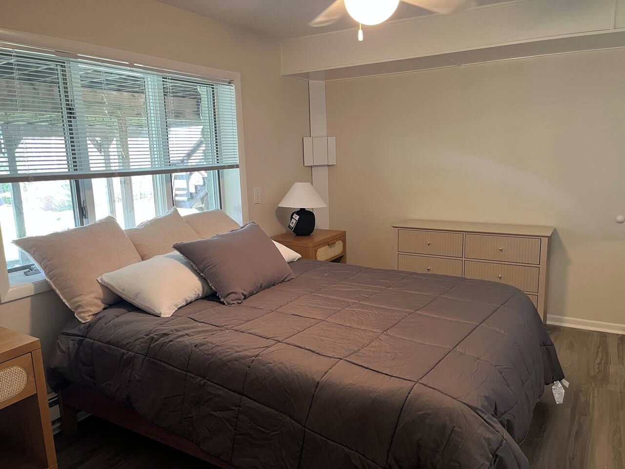 A bedroom with a bed, bedside table, lamp, and a dresser.