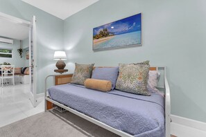 A bedroom with a bed, pillows, a nightstand, a lamp, a window, and a painting of a beach scene. - 5 bedroom/ 3 Bathroom Tropical Resort w/Gym near Pompano Beach and Parks (Pompano Beach)