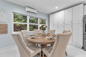 A modern kitchen with white cabinets, a dining table set for six, and a large window overlooking a garden. - 5 bedroom/ 3 Bathroom Tropical Resort w/Gym near Pompano Beach and Parks (Pompano Beach)