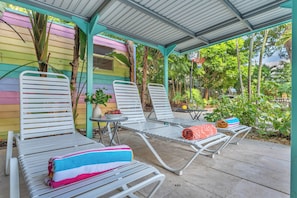 Un espace extérieur abrité avec des chaises et une table en métal blanc, un panier de basket et, en arrière-plan, un bâtiment aux couleurs vives.