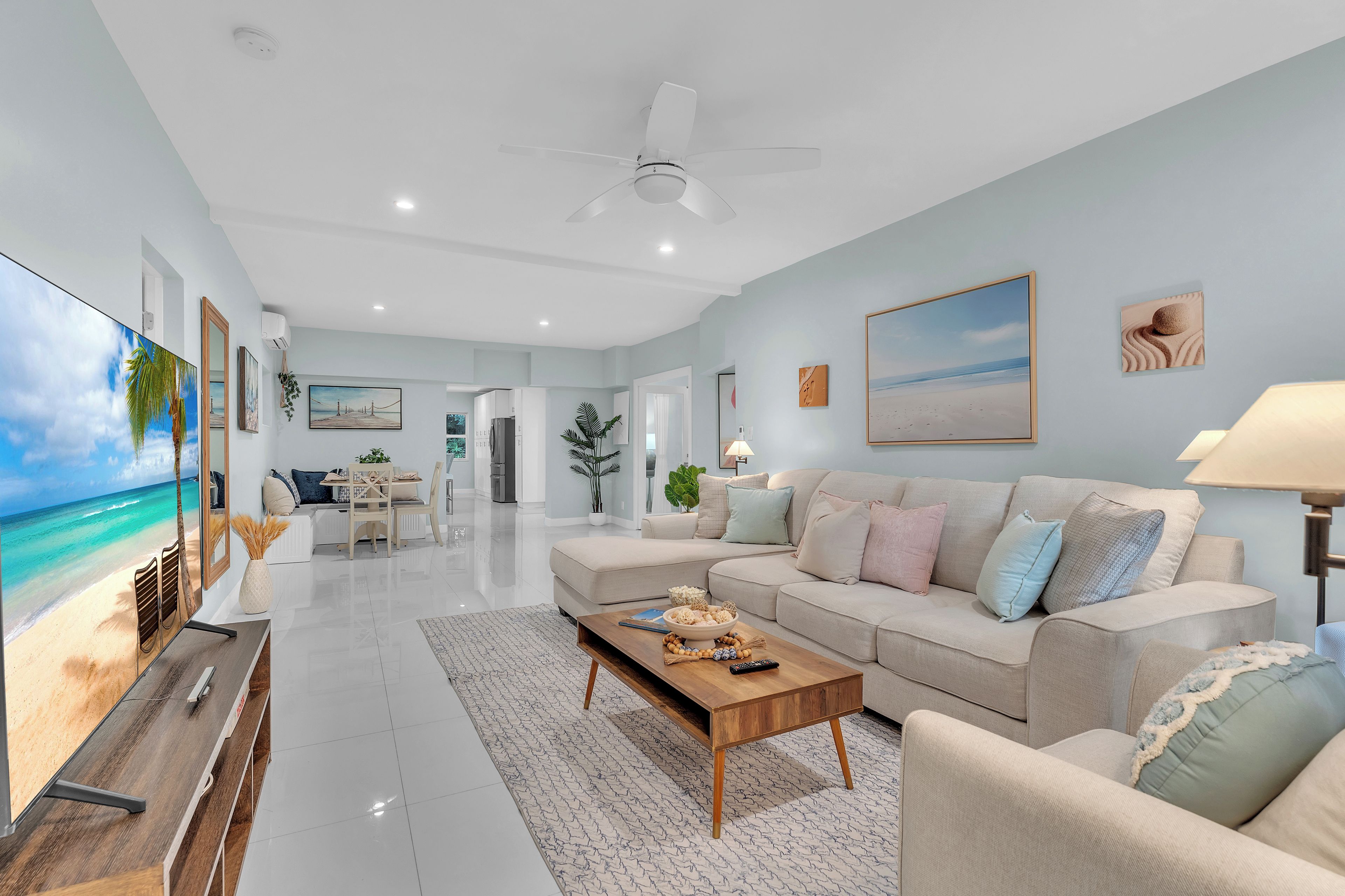 A modern living room with a large flat-screen TV, a sofa set, a coffee table, and a ceiling fan.