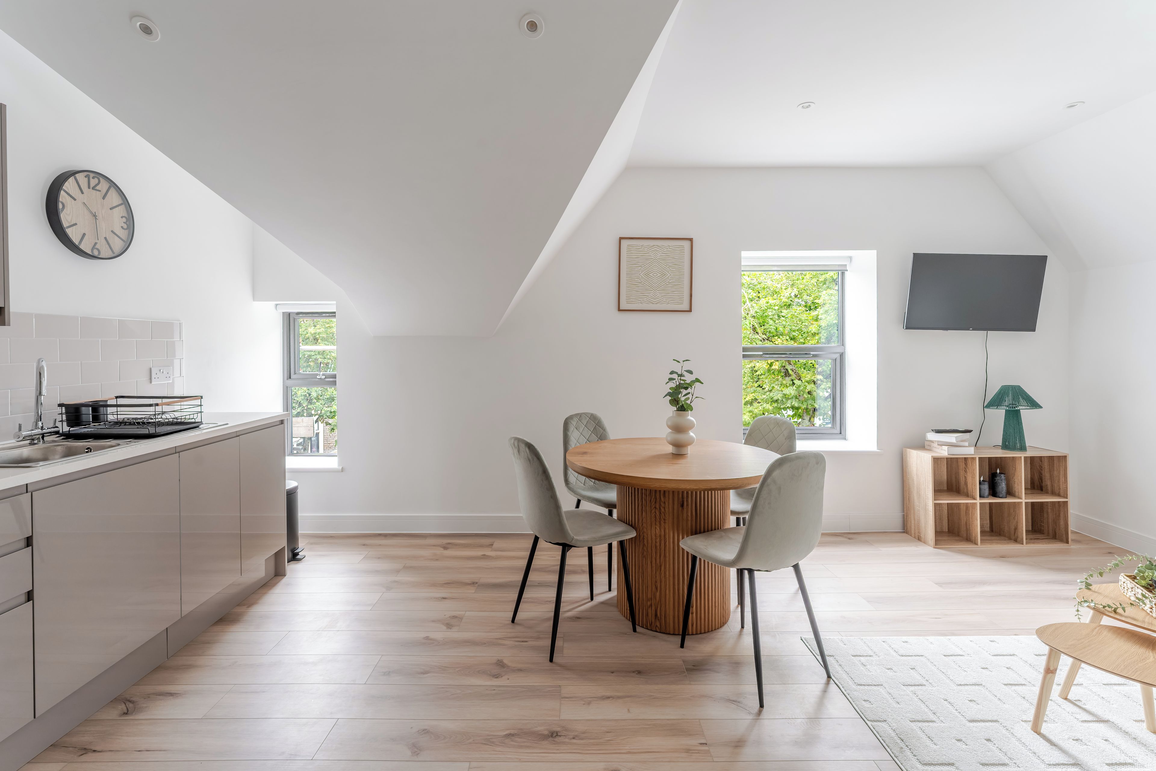 A modern kitchen with a dining area, wooden flooring, and a large window.