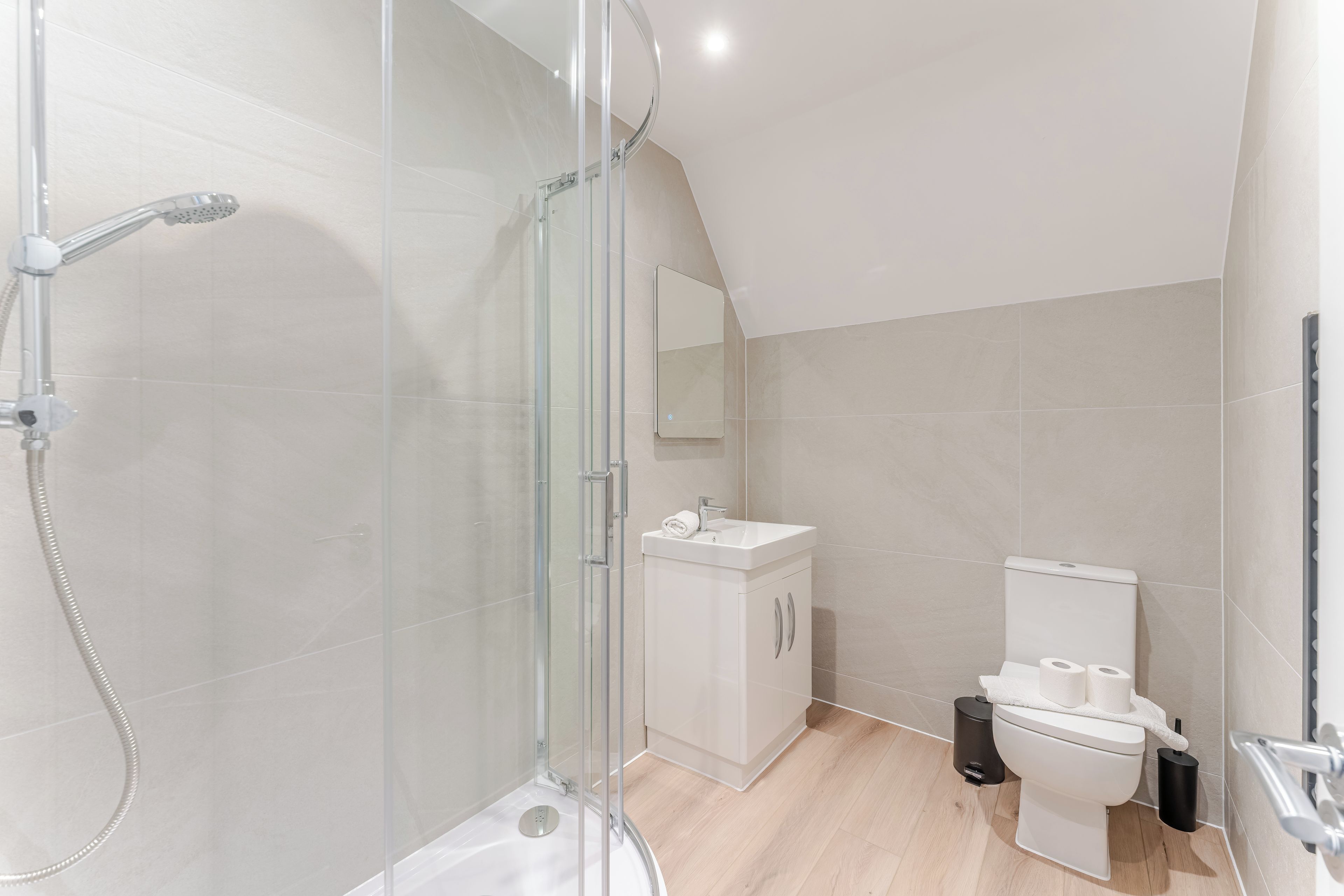Et moderne badeværelse med en glasbrusekabine, en hvid vask og et toilet.
