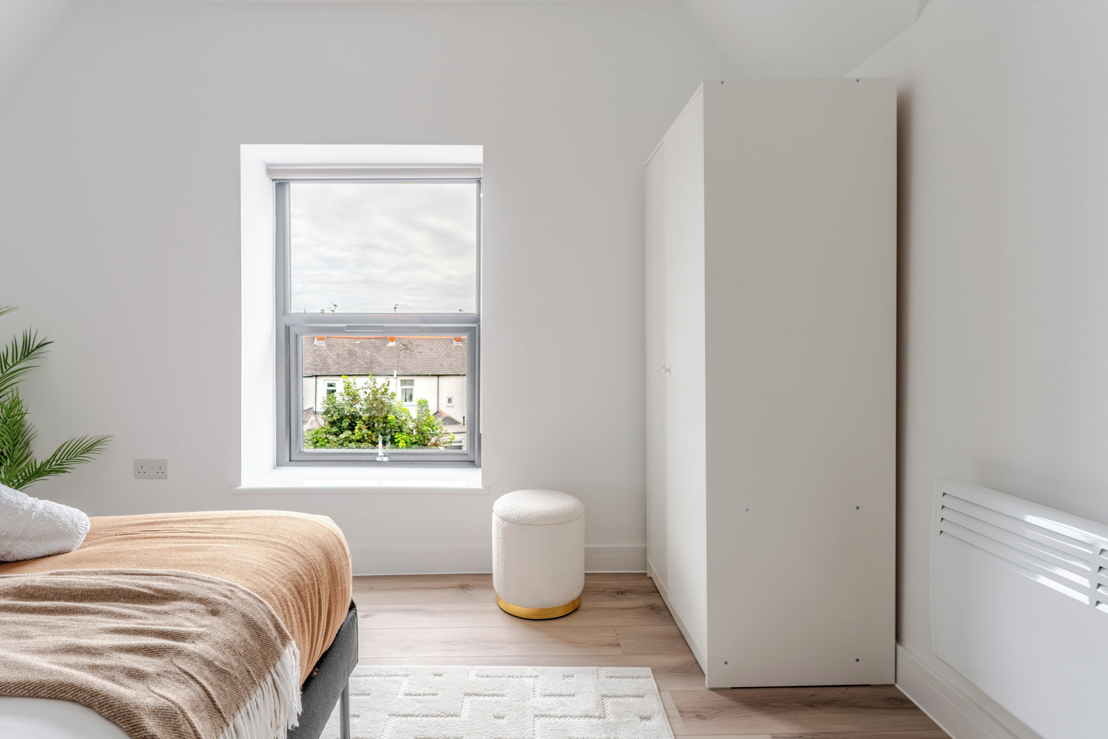 A bedroom with a bed, a window, a radiator, and a plant.