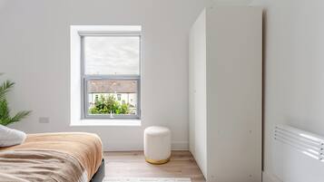 A bedroom with a bed, a window, a radiator, and a plant.