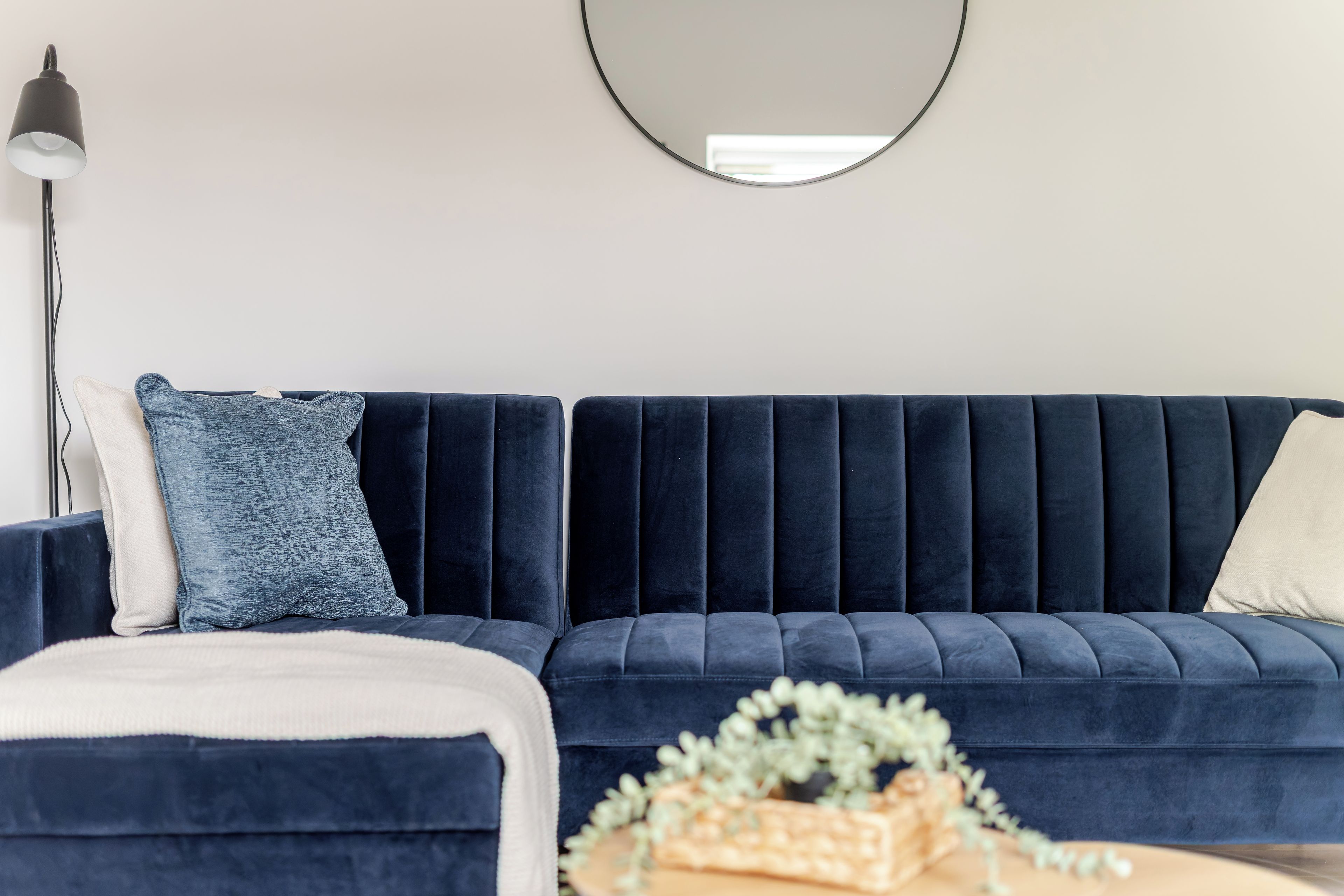 A dark blue sofa with a tufted backrest, a matching ottoman, and a round mirror on the wall.