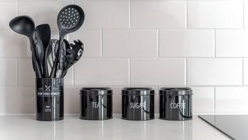 A kitchen counter with a utensil holder and three labeled containers for tea, sugar, and coffee.