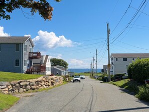 A residential street with houses, a stone wall, and a clear sky. - Spacious 5-bedroom House Walk to Scarborough Beach! (Narragansett)