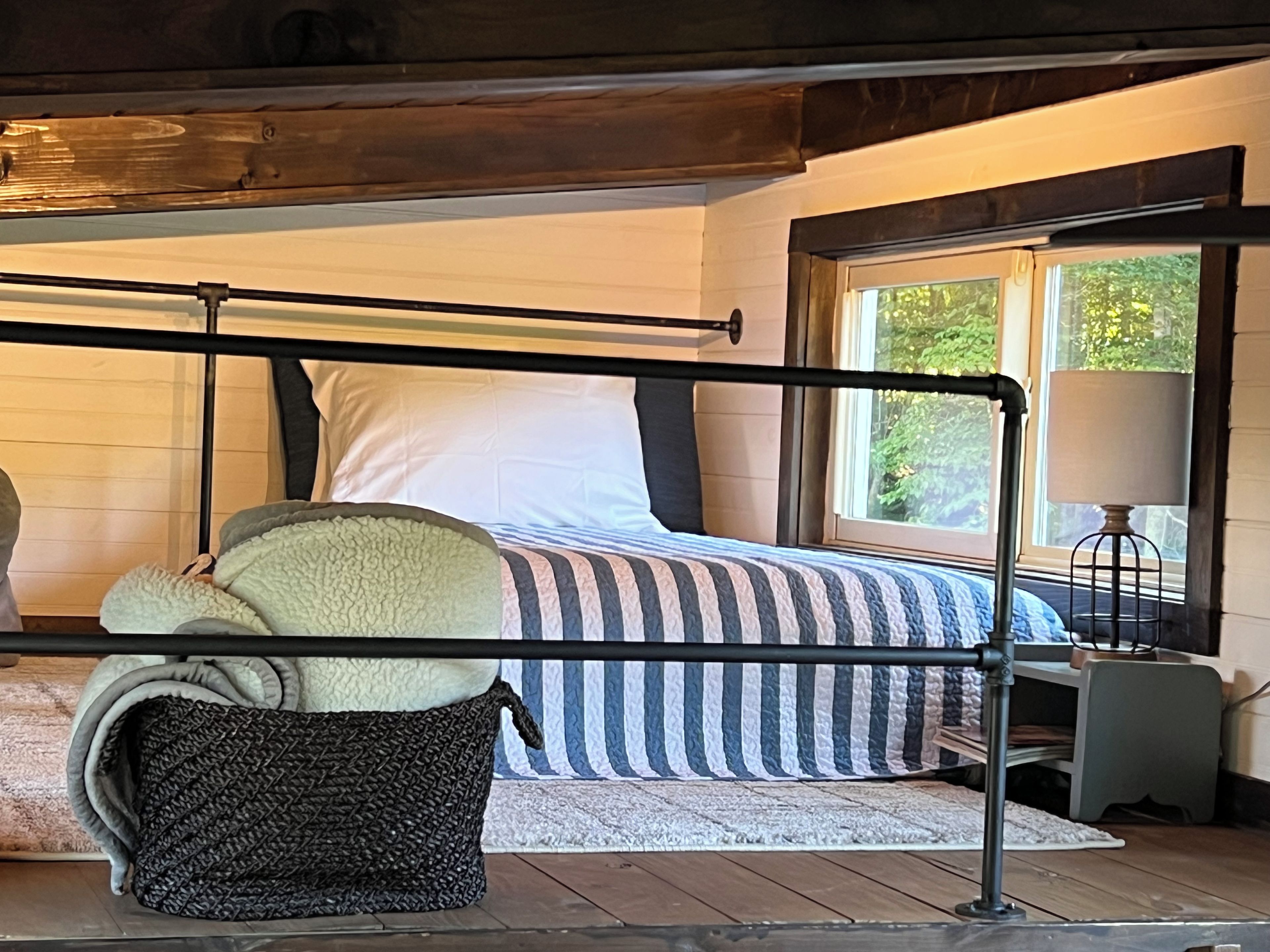 Ein Schlafzimmer mit Bett, Fenster, Lampe und Korb.