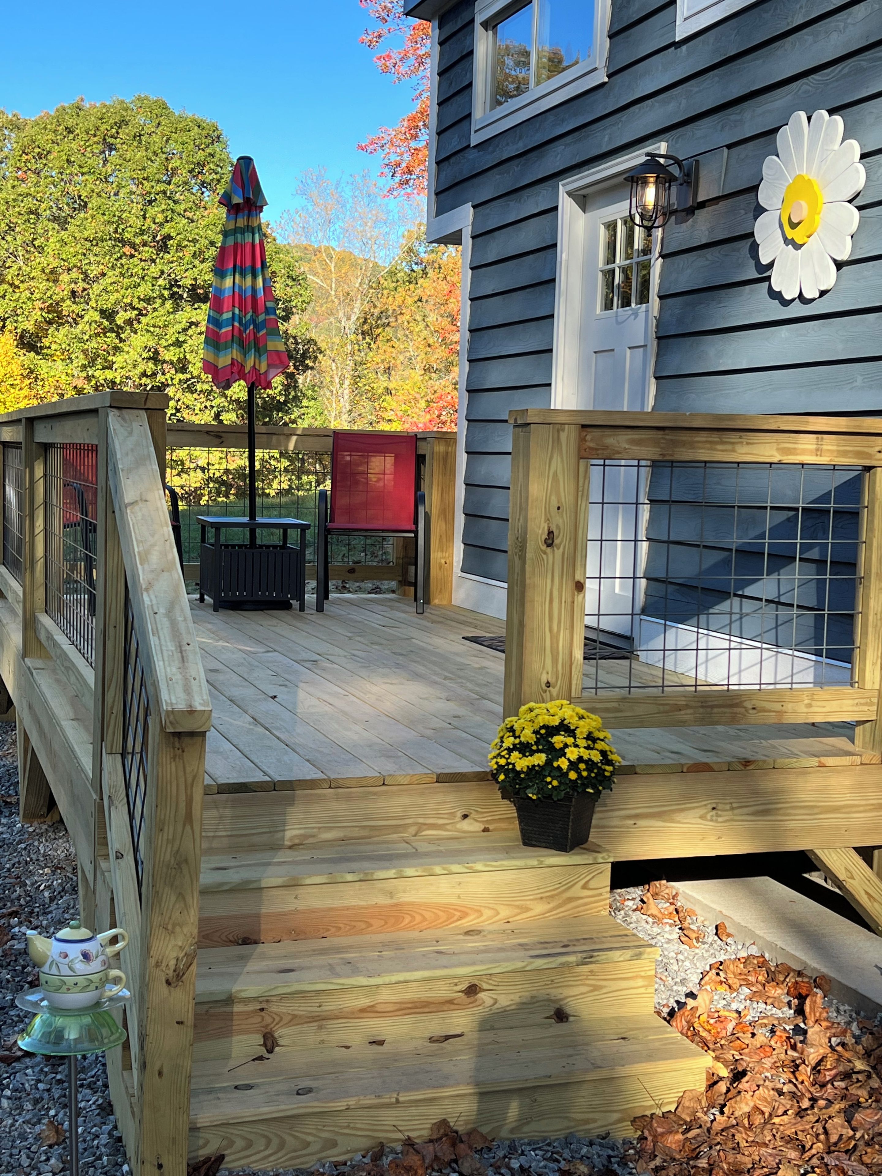 A wooden deck with a railing, a potted yellow flower, and a red umbrella.