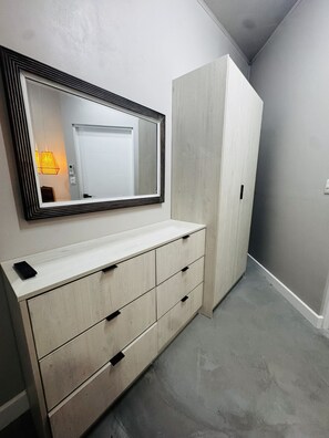Ein Zimmer mit einem weißen Kleiderschrank, einem Schminkspiegel an einem Schrank und einer hellen Kommode mit Schubladen.