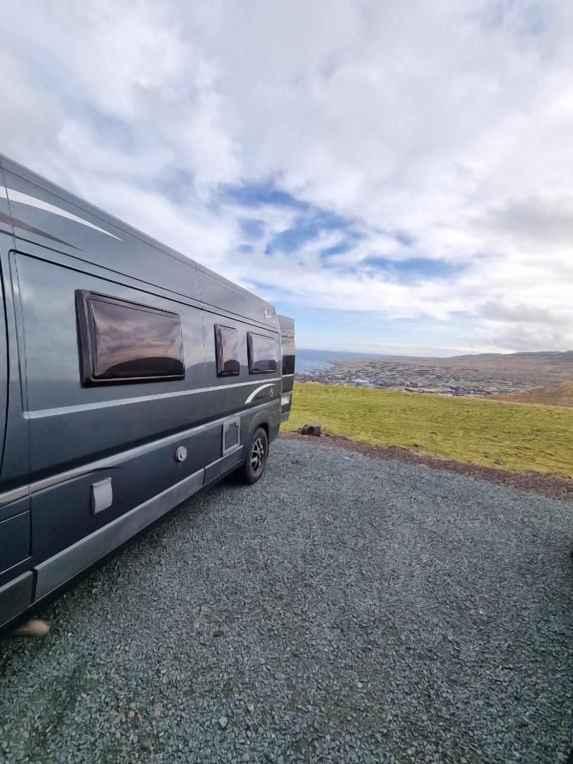 A stationary RV parked on a gravel surface with a view of a grassy field and distant landscape.