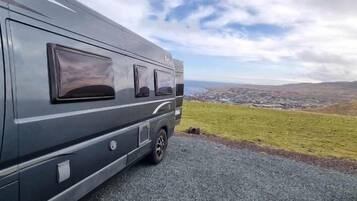 A stationary RV parked on a gravel surface with a view of a grassy field and distant landscape.