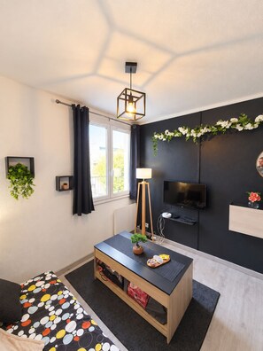 Un saló modern amb una decoració en blanc i negre, un televisor de pantalla plana penjat a la paret, una taula baixa de fusta amb una planta i un gran finestral amb cortines.