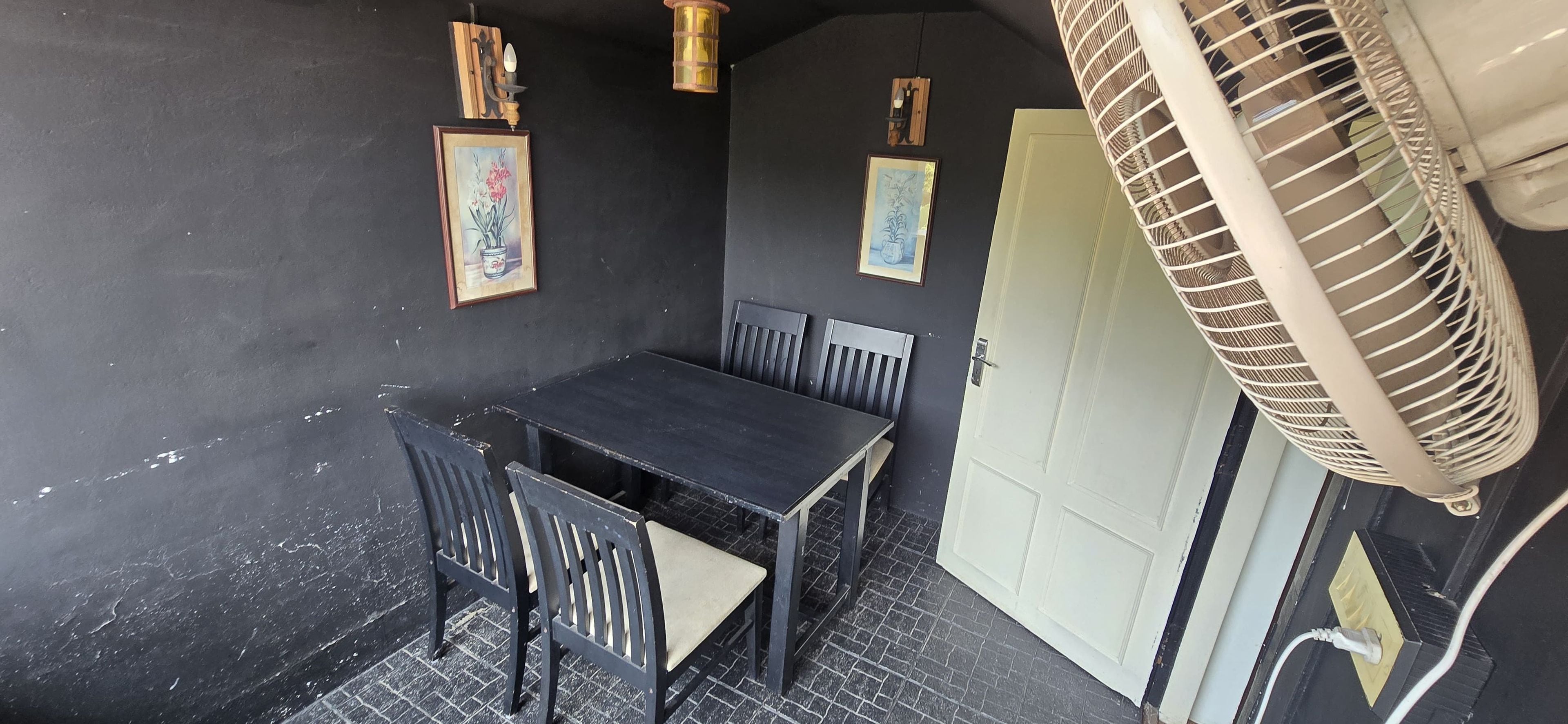 Une pièce avec une table et des chaises, un ventilateur et deux tableaux encadrés accrochés au mur.