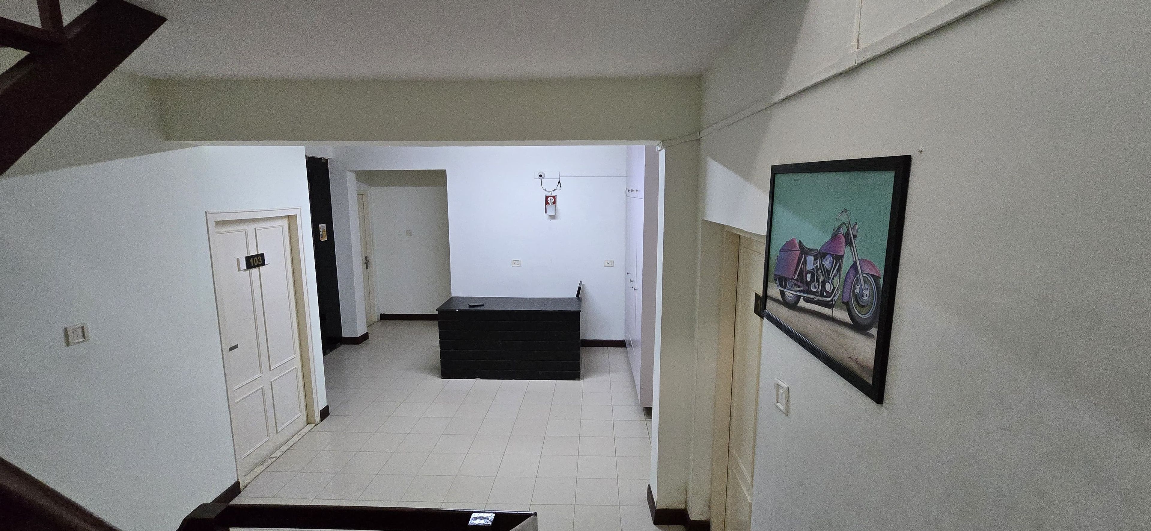 A hallway with a door labeled '103,' a black bench, and a framed picture on the wall.