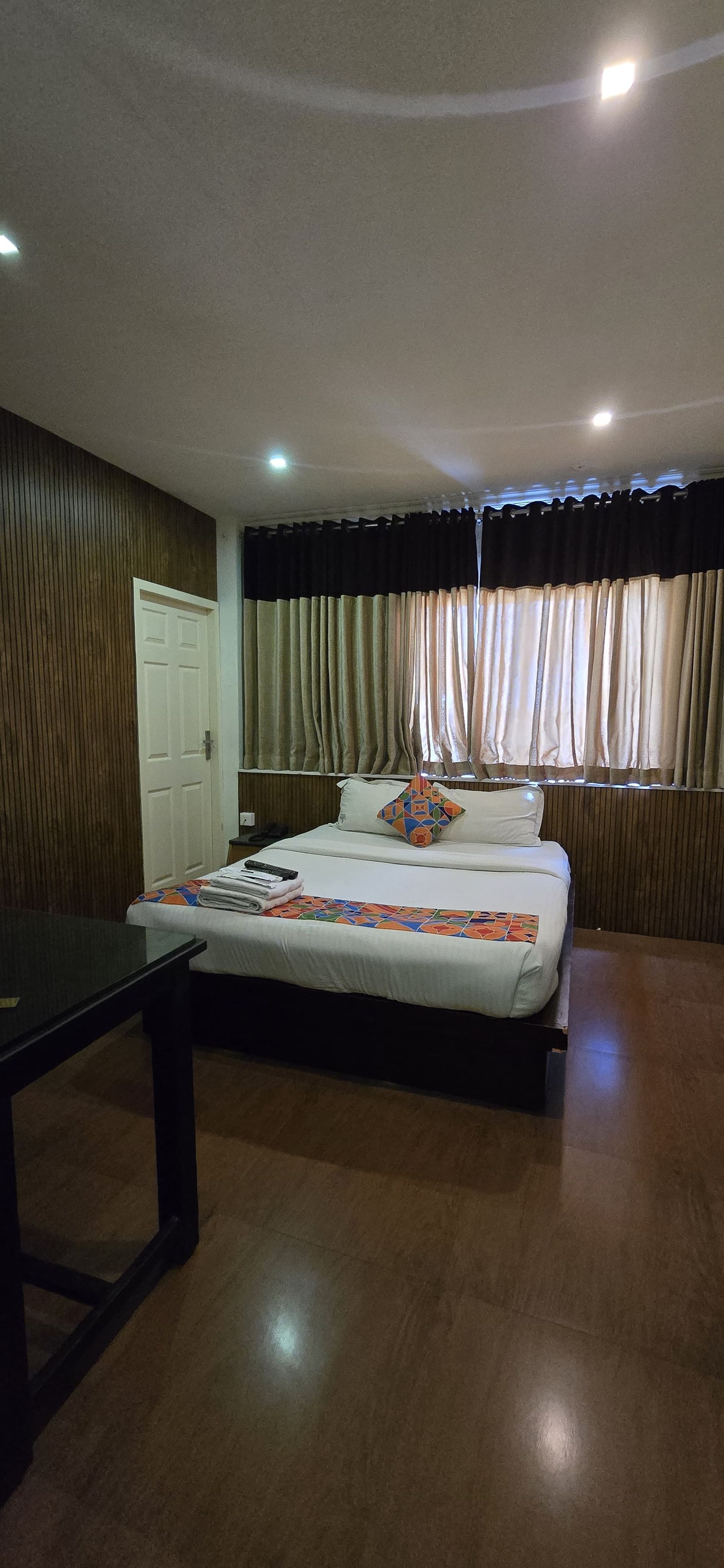 Una habitación de hotel con una cama, una mesita de noche, un escritorio y una ventana con cortinas.