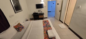 A hotel room with a bed, a desk, a television, and a bathroom door.