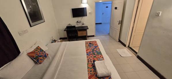 Une chambre d’hôtel avec un lit, un bureau, une télévision et une porte de salle de bain.