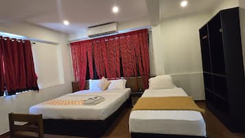 A hotel room with a bed, a bedside table, a chair, a wardrobe, and a window with red curtains.