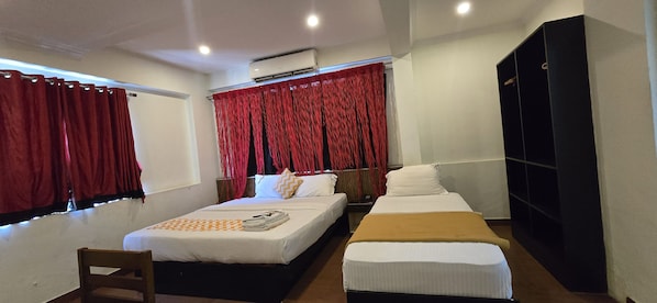 Habitación de hotel con cama, mesita de noche, una silla, armario y ventana con cortinas rojas.