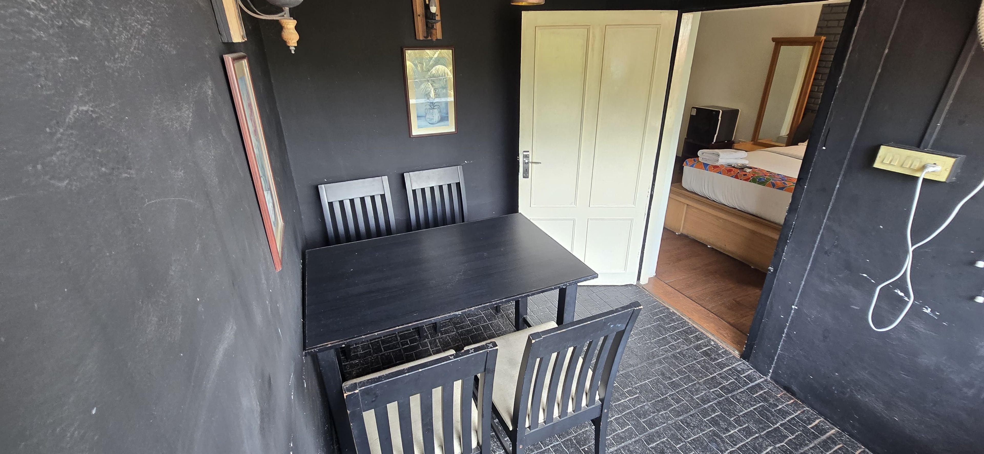 A room with a black table and chairs, a white door, and a bed with a colorful mattress.