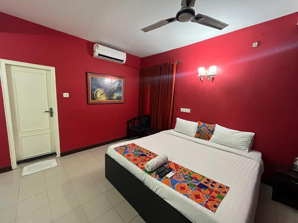 Une chambre d’hôtel avec un lit, un ventilateur de plafond, un appareil de climatisation, une porte et un tableau au mur.