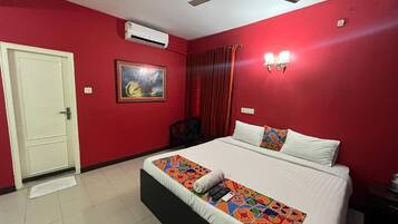 Une chambre d’hôtel avec un lit, un ventilateur de plafond, un appareil de climatisation, une porte et un tableau au mur.