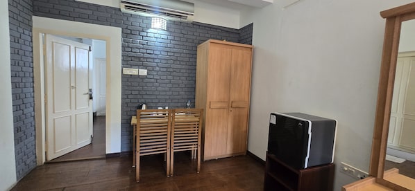 A room with a brick wall, a wooden wardrobe, a television on a stand, and a door leading to another room.