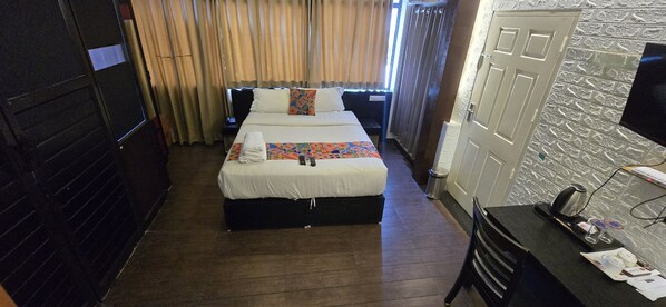 A narrow hotel room with a bed, a desk, and a chair.
