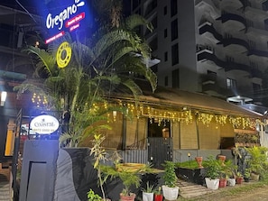 A hotel with a sign for 'Oregano' and 'Coastlab' indicating nearby locations. There are potted plants and a palm tree in the foreground.