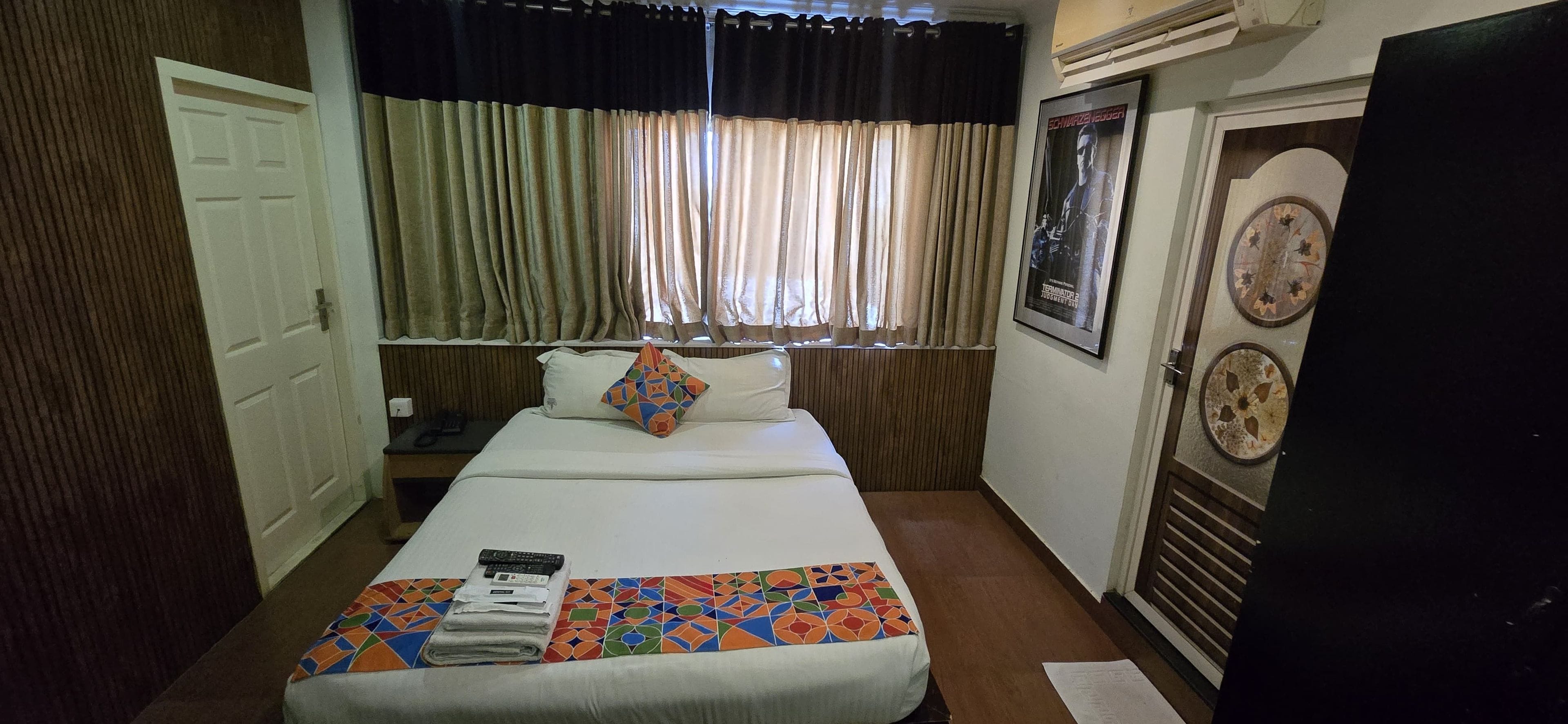 Una habitación de hotel con cama, ventana con cortinas, un reloj de pared y un cuadro enmarcado.