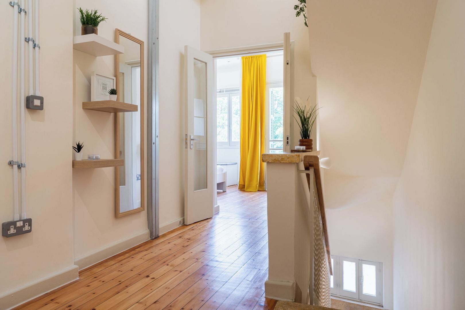 Un couloir doté d’un plancher en bois, d’une porte blanche et d’un rideau jaune vif.