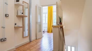 Un couloir doté d’un plancher en bois, d’une porte blanche et d’un rideau jaune vif.