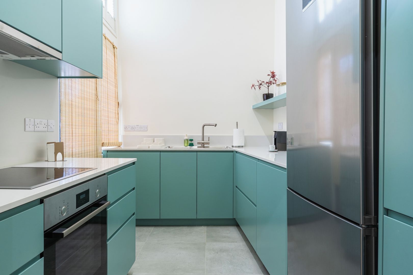 Una cucina moderna con mobili color petrolio, un frigorifero in acciaio inossidabile e un forno integrato.