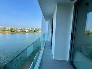 A balcony with a glass railing overlooking a body of water and distant buildings. - Laguna luxury Living, Stunning 1-Bedroom Waterfront Escape (Phuket)