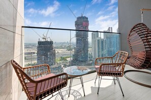 Ein Balkon mit Glasgeländer, zwei Korbstühle und einem runden Tisch.