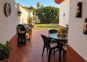 Eine Terrasse mit rundem Tisch und Stühlen, einem Grill und Kübelpflanzen.