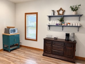 A kitchen with a microwave on a teal cabinet, a coffee maker on a wooden cabinet, and a window with blinds.