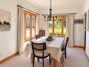 Comedor con una mesa dispuesta para cuatro, una araña y vistas a un jardín a través de amplios ventanales.