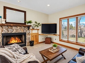 Una sala de estar con chimenea de piedra, un televisor de pantalla plana, un ventanal con persianas y una zona de estar acogedora.